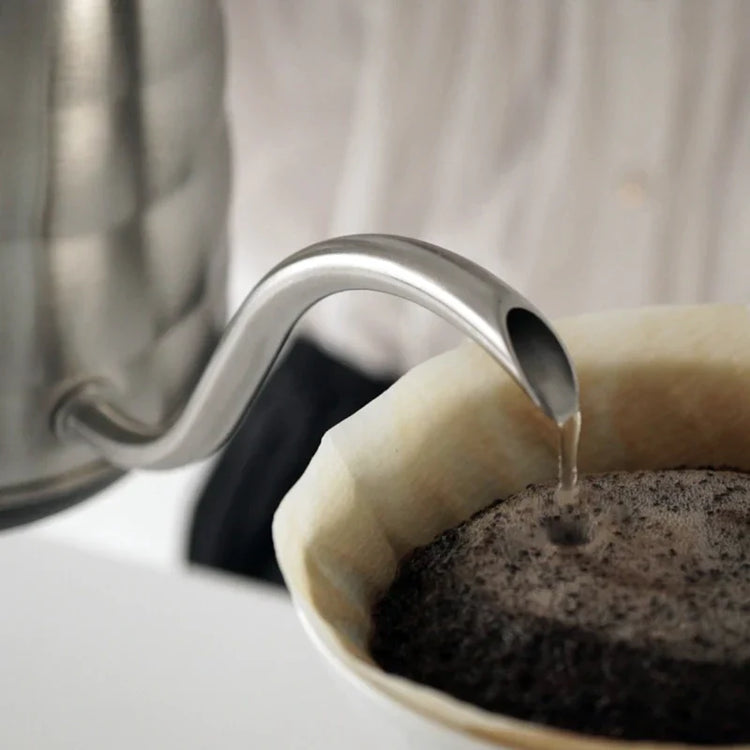 Nærbillede af en metalkedel, der hælder varmt vand over kaffegrums i et filter, og dampen stiger op, mens brygningen begynder.