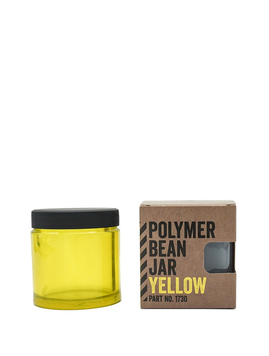 En gennemsigtig gul Comandante polymer krukke mærket "Polymer Bean Jar med låg, Gul" med sort låg er ved siden af en brun æske. Den fede tekst på æsken lyder "POLYMERBØNNEKRUDE GUL DEL NR. 1730", hvilket sikrer, at det er fødevaresikker til sikker opbevaring.