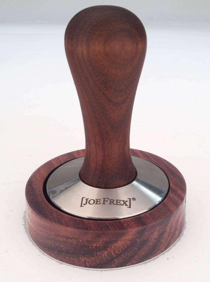 Joe Frex stamper-stationen har en valnødtræ-håndtaget tamper med en poleret metalbund, indgraveret med "Joe Frex", essentiel for kaffeudstyr i espressotilberedning. Den står oprejst på hvidt, eventuelt i nærheden af en stamperholder til ryddig opbevaring.