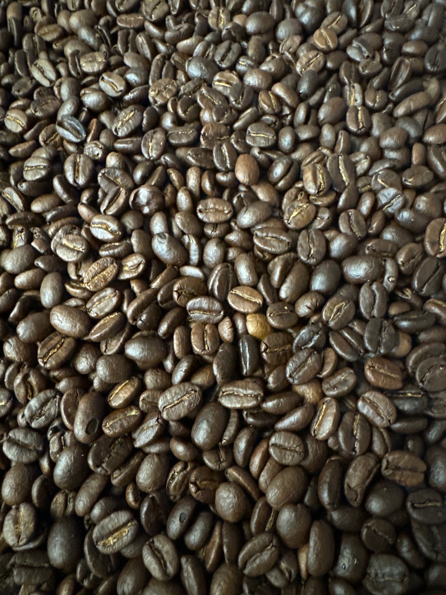 Et nærbillede af en stor bunke EverBeans No. 06 · Colombia Dark Roast bønner afslører deres blanke, mørkebrune udseende, hvilket fremhæver deres rige tekstur og varierende størrelse.