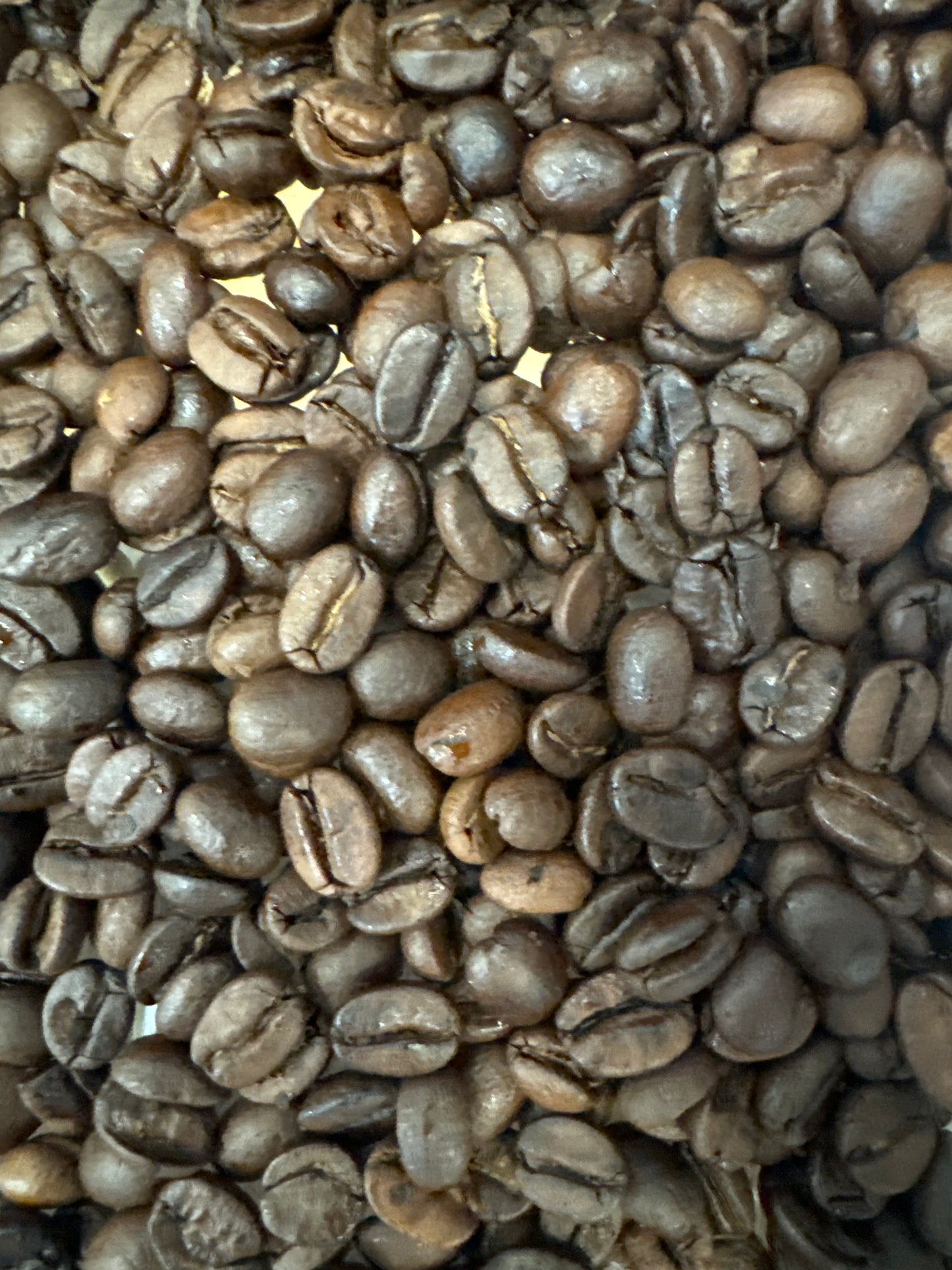 Et nærbillede af blanke, ovale ristede kaffebønner fra EverBean's No. 04 · Colombia Decaf fremhæver forskellige nuancer af brunt og karakteristiske riller, der inkarnerer en perfekt blanding af aroma og kunstnerisk karakter, der minder om rig colombiansk kaffe.