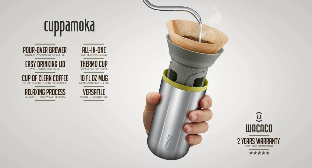 En hånd holder Wacaco Cuppamoka, en slank sølvfarvet pour-over-kaffemaskine med metalsugerør og papirfilter. Varmt vand hældes i. Funktionerne omfatter et låg, der er let at drikke, en termokop og 2 års Wacaco-garanti - i bærbar kaffebrygger.