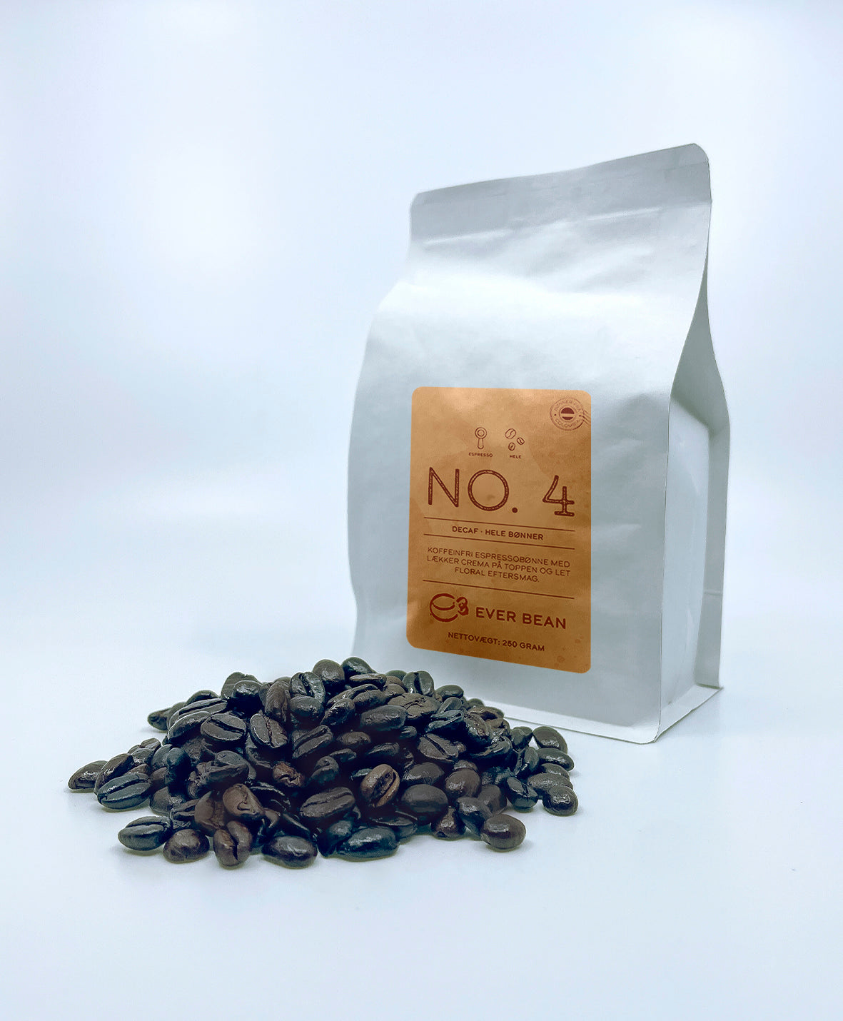 En hvid EverBean-pose mærket "No. 04 · Colombia Decaf, Whole Beans" dukker op ved siden af en bunke mørkristede kaffebønner med branding og vægtdetaljer på en almindelig hvid baggrund.