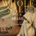 Jutesække mærket "Brasilien" stablet sammen med en fed gul tekst, hvor der står "WHOLESALE No. 02 - Brasilen (øko) (w)" og EverBean Wholesales logo - med hele Arabica kaffebønner fra Brasilien.