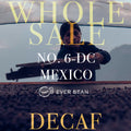 En person spreder hele bønner på et tørrestativ under en baldakin. Overlejret tekst: "EVERBEAN WHOLESALE NO. 06-DC MEXICO DARK ROAST, DECAF (ØKO) (W)." Perfekt til dem, der søger autentisk mexicansk kaffe uden koffein.
