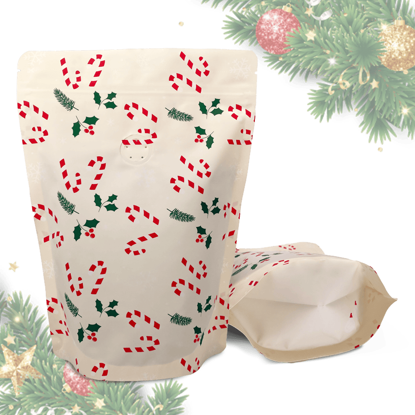 To fødevaregodkendte EverBean Kaffe pose, emballage med ventil stand-up pouches med julemotiver af sukkerrør, kristtjørn og fyrretræsgrene - den ene stående, den anden liggende. Juletræsgrene og pynt pynter i baggrunden.