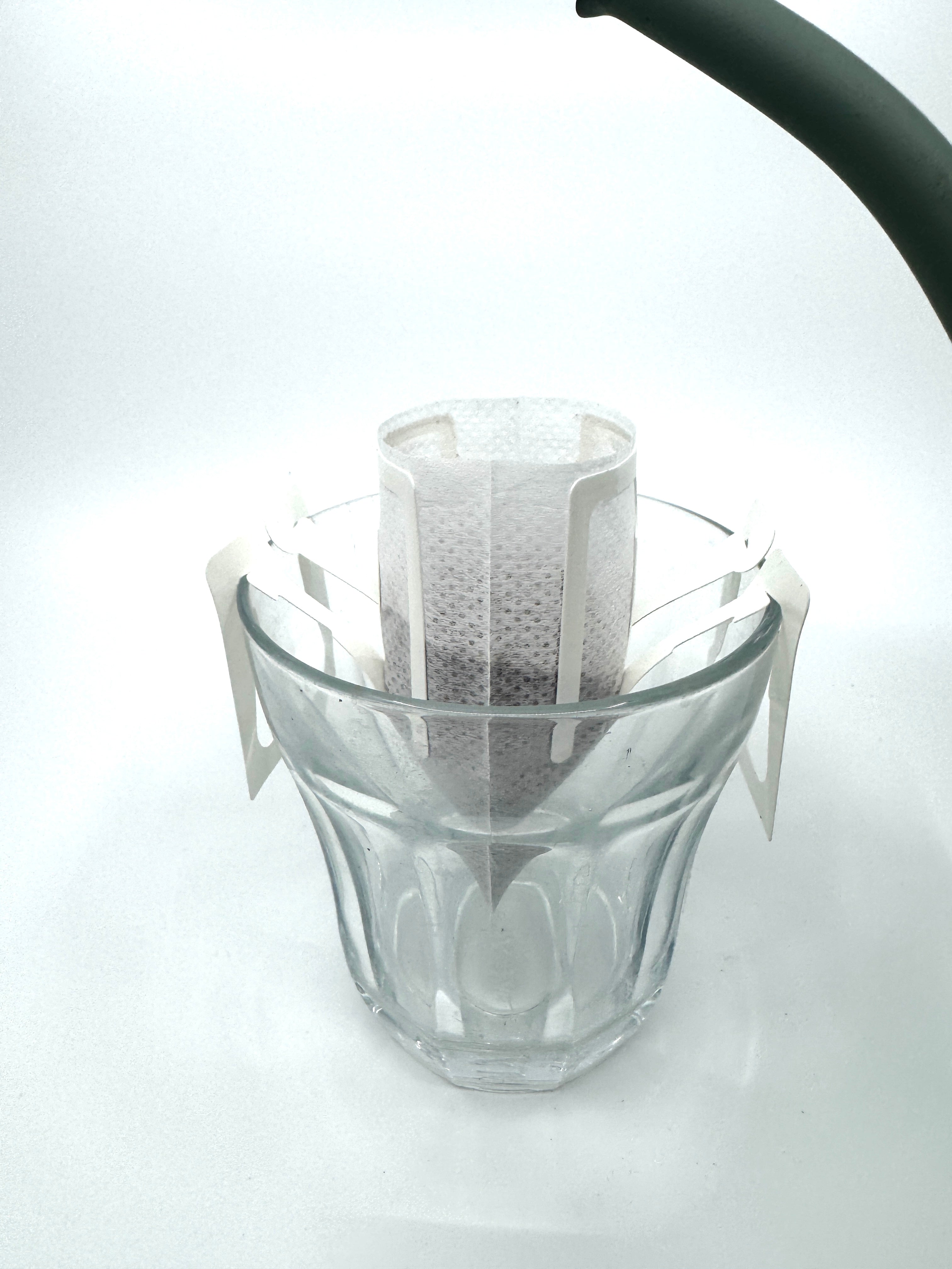Et No. 08 - Etiopien, Single Serve drypkaffefilter fra EverBean ApS. fyldt med malede bønner sidder over et glas, mens en kedeltud svæver over, klar til at hælde varmt vand i det ventende filter.