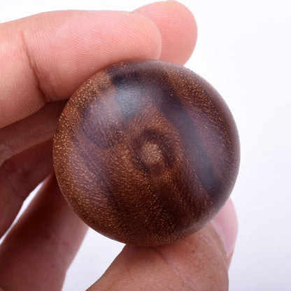 En hånd holder en glat, rund træknop i rig brun med synlige åremønstre, der minder om Joe Frex's stamper-design. Den almindelige hvide baggrund fremhæver håndværket af Joe Frex Classic Short Handle i udsøgt valnød.