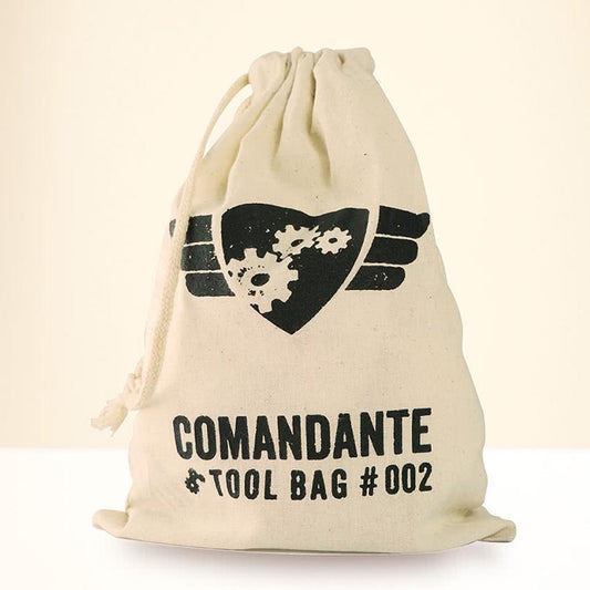 En beige Comandante, Barista Tilbehørs Pose #2 med et sort emblem af tandhjul og vinger. "COMANDANTE # TOOL BAG #002" under fremhæver dens kaffepassion, der sidder elegant på en neutral baggrund.
