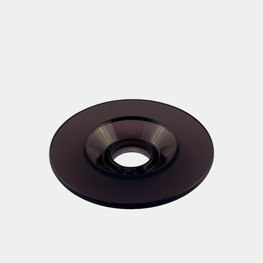 Et blankt, sort glasobjekt fra Comandante, X25 Låg Sort, er donutformet med et centralt cirkulært hul og sat mod en almindelig, lysegrå baggrund.