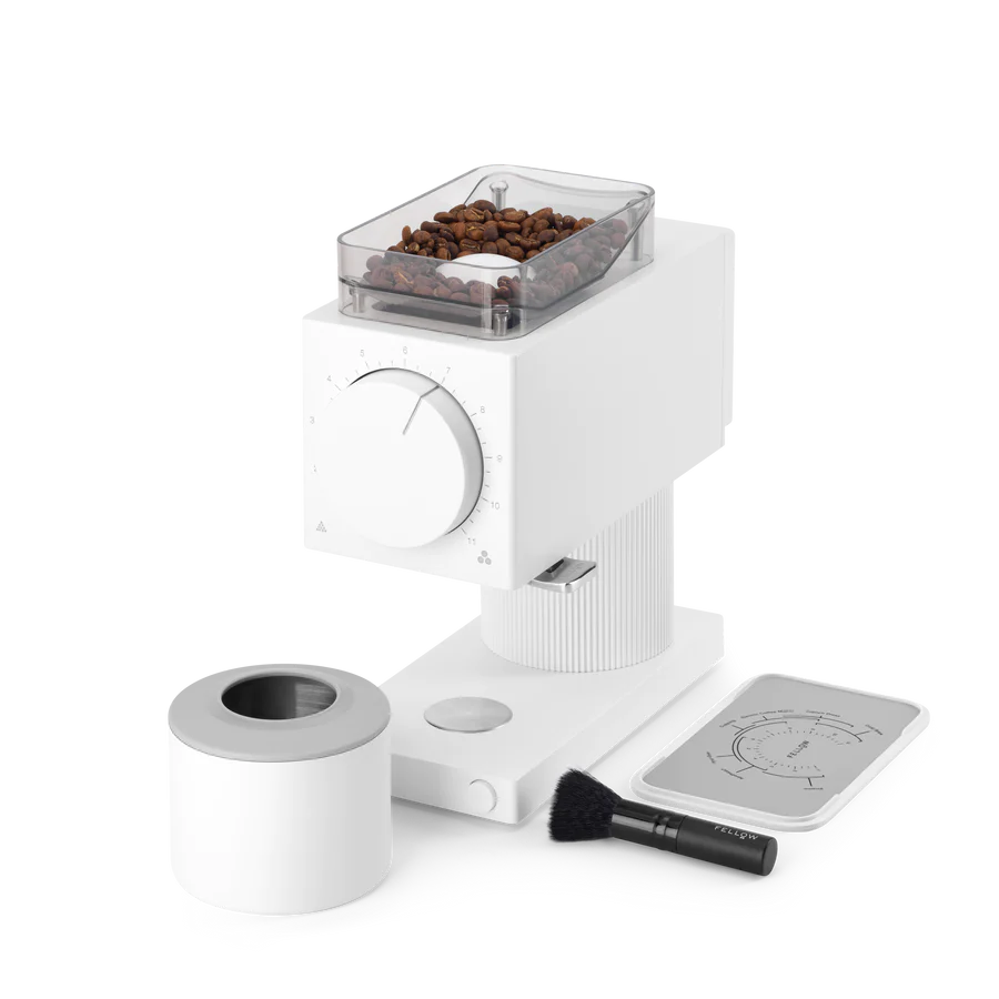 Fellow Ode Brew Gen 2 Kværn vises med kaffebønner i dets øverste rum og en stor frontskive. Ved siden af er et hvidt låg, børste og et instruktionskort med diagrammer på kaffebryggemetoden.