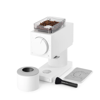 Fellow Ode Brew Gen 2 Kværn vises med kaffebønner i dets øverste rum og en stor frontskive. Ved siden af er et hvidt låg, børste og et instruktionskort med diagrammer på kaffebryggemetoden.