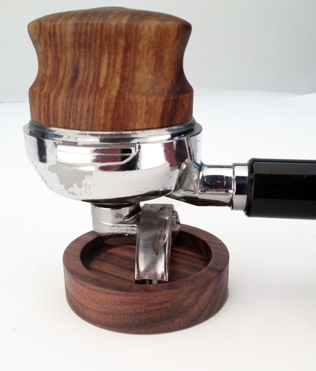 Joe Frex Stamper Station, Valnød viser et elegant portafilter med et træhåndtag, dygtigt udformet af valnødtræ. Placeret på hovedet på sin matchede holder, fremhæver de skinnende metaldele smukt både træ- og metalteksturer mod en lys baggrund, hvilket harmoniserer kaffeudstyr.