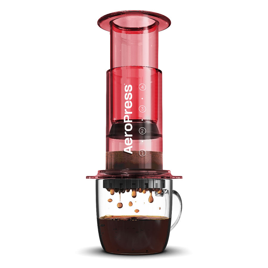 En rød AeroPress, Limited, Kaffebrygger fra Aeropress sidder på et klart glaskrus, mens kaffen drypper gennem filteret - ideelt for fans af innovativ bryggeteknologi.