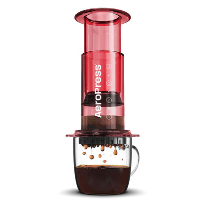 En rød AeroPress, Limited, Kaffebrygger fra Aeropress sidder på et klart glaskrus, mens kaffen drypper gennem filteret - ideelt for fans af innovativ bryggeteknologi.