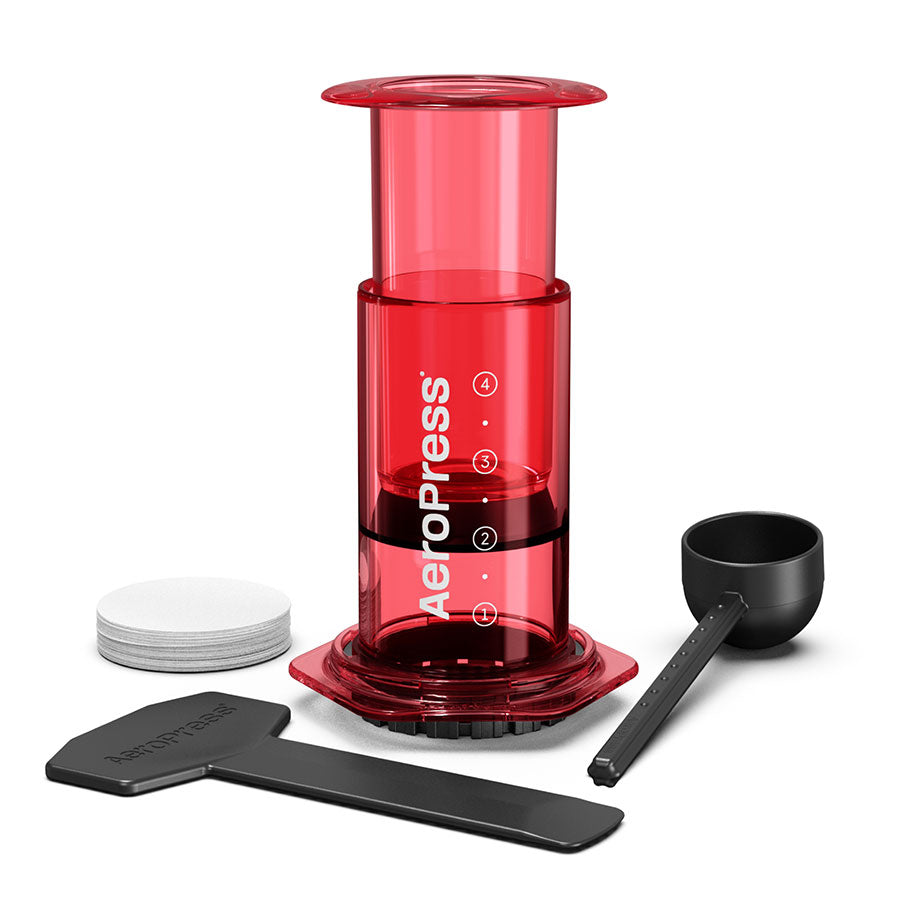 AeroPress, Limited, Kaffebrygger by Aeropress i rød har avanceret bryggeteknologi og inkluderer en kaffepresse, scoop, omrører og runde papirfiltre - alt sammen vist på en hvid baggrund.