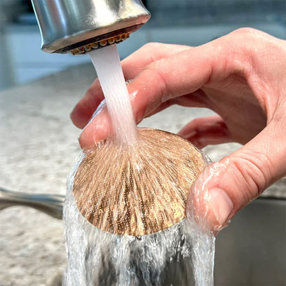 En hånd holder en rund kobberskrubbe under en køkkenhane for at rengøre den - ligesom når man skyller et AeroPress Gold Tone-filter fra Aeropress i vasken efter brug.