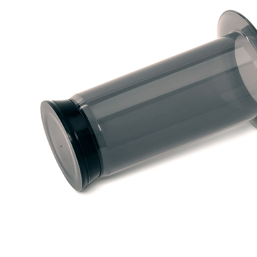 Et gennemsigtigt cylindrisk Aeropress gummistempel med sorte endestykker er placeret vandret mod en almindelig hvid baggrund.