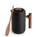 Den slanke sorte Fellow Clara French Press, Valnød har vakuumisolerede vægge for optimal varmetilbageholdelse. Dets moderne design er fremhævet af et træhåndtag og låg, med en træspatel lænet mod det på en almindelig baggrund.
