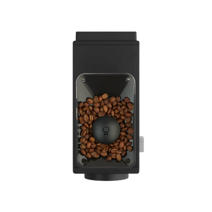 Set ovenfra af en Fellow Ode Brew Gen 2 Kværn kaffekværn fyldt med brune bønner. Det slanke sorte rektangulære design har antistatisk teknologi og et gennemsigtigt vindue, der viser bønner omkring den centrale slibemekanisme.
