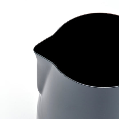 Et nærbillede af Rhino Coffee Gear Stelth Milk Pitcher i sort med en tud til latte art, set ovenfra og i en vinkel mod en hvid baggrund.