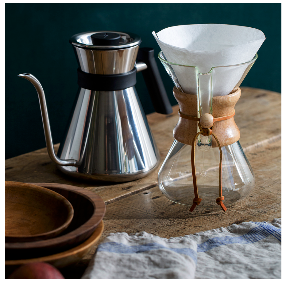 En Chemex-brygger med Chemex Kaffefiltre står på et træbord ved siden af træskåle og en blåstribet klud.