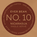 På en cirkulær kaffeetiket står der: "EverBean ApS. No. 10 Nicaragua, Single Serve." Rundt i kanten: "100% Arabica kaffebønner fra Sajonia Estate Coffee - nicaraguansk kaffe, nydes på farten eller i værtshjem.