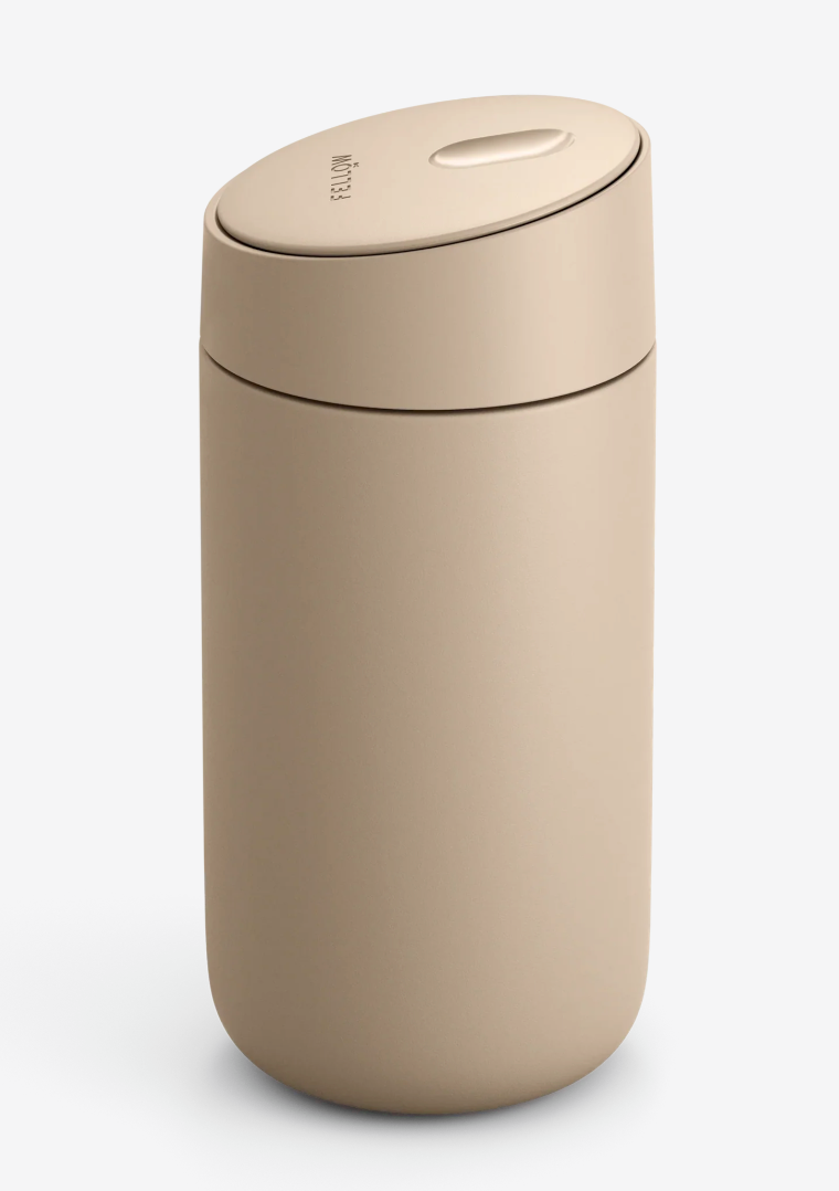 En beige, mat Fellow Carter Slide Mug termo krus med en afrundet krop, let hvælvet skydelåg og keramisk belægning vises mod en almindelig hvid baggrund.