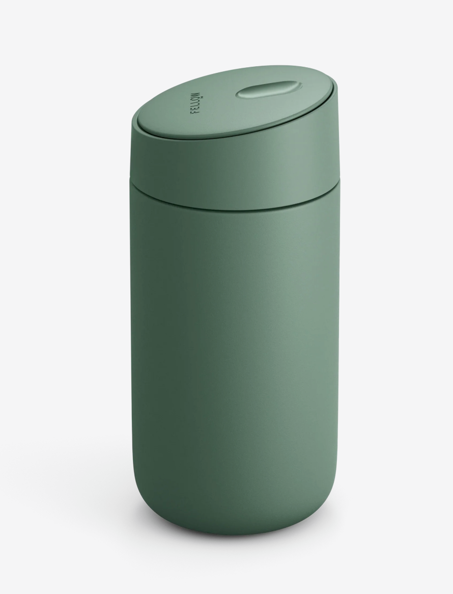 Et matgrønt, cylindrisk Fellow Carter Slide Mug termo krus fra Fellow med keramisk belægning, afrundet låg og en lille oval knap på toppen på en almindelig hvid baggrund.