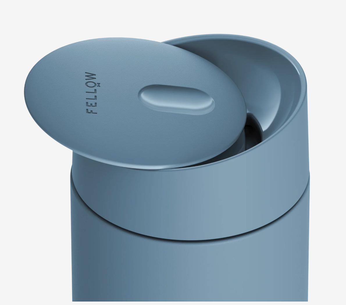 Et nærbillede af et lyseblåt Fellow Carter Slide Mug med låget let åbent, så man kan se drikkeåbningen. "FELLOW" er trykt på låget og fremhæver dets termokrusdesign, så man kan nyde drikkevarer på farten.