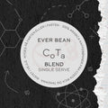 På en rund kaffeetiket på en struktureret sort-hvid baggrund står der: "EverBean ApS. Single Serve, CoTa." På kanten står der 100% Arabica Tanzania kaffe og dansk vejledning. Videnskabsinspirerede skitser tilføjer visuel flair.