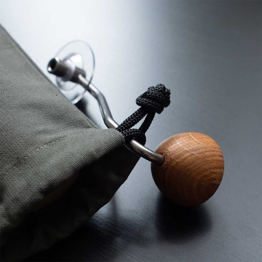 Et nærbillede af Comandante Toolbag #5 fra Comandante, fremstillet af mørkt bomuldslærred med en metal- og trælukning og en knudret sort snor - ideel til opbevaring af kaffeudstyr eller som Comandante-værktøjstaske.