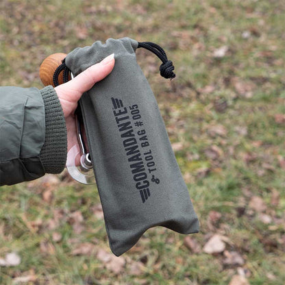 En person holder en grøn Comandante Toolbag #5 fra Comandante, lavet af bomuldscanvas, udendørs blandt græs og nedfaldne blade - en ideel kaffegrej-opbevaringsløsning.