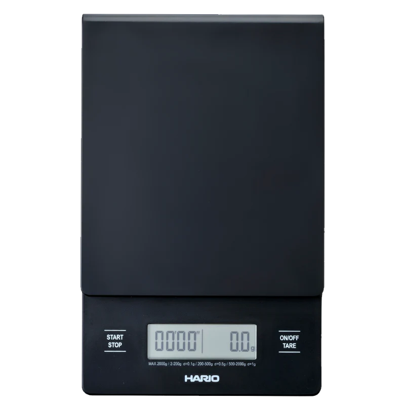 Hario V60 Drip Vægt er en digital køkkenvægt perfekt til præcis pour-over brygning, med en slank sort overflade og rektangulært design. Den har et display, der viser "0000" og "0.0", med "Start/Stop" og "On/Off Tare"-knapper, der viser det berømte Hario-mærke under skærmen.