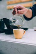 Der skænkes kaffe fra en glaskaraffel i en lille gul kop under en kaffesmagning arrangeret af EverBean ApS.