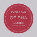 En rød cirkulær kaffeetiket med hvid tekst lyder: "EverBean Limited Single Serve, Limited, Columbia Geisha." Rundt om kanten står der: "100% Arabica kaffebønner fra Colombia. Ristet i Norge. Nydes på farten eller i farten.
