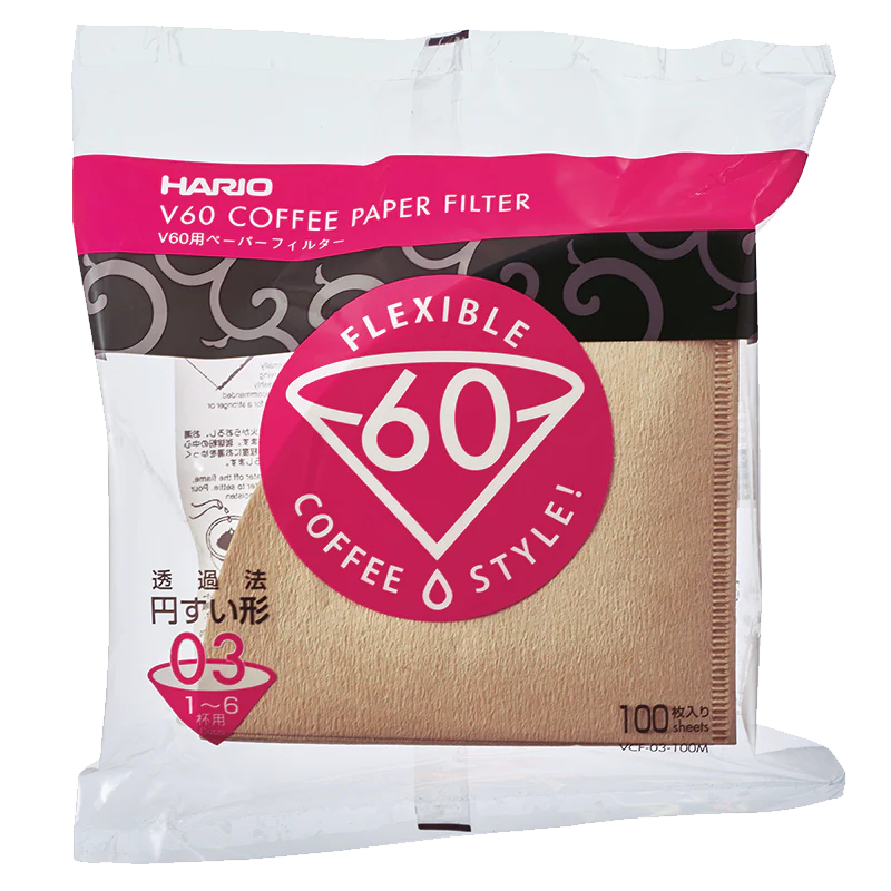 En pakke med 100 Hario Papirfiltre, naturbrune kegleformede kaffefiltre (størrelse 03), biologisk nedbrydelige, i klar plastfolie med pink og hvid "FLEXIBLE V60 COFFEE STYLE!"-etiket. Mærke: Hario.