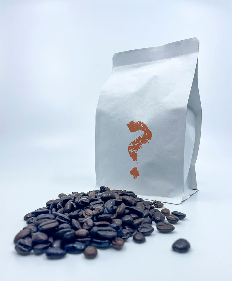 En hvid EverBean "Giv et gavekort"-pose med et orange spørgsmålstegn står oprejst bag spredte ristede kaffebønner på en hvid baggrund og hentyder til et overraskelsesgavekort fra din yndlingswebshop.