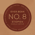 En brun cirkulær etiket centrerer teksten "EverBean Single Serve" og langs kanten står "100% Arabica kaffebønner fra Etiopien" plus "Nydes på farten eller i farten", hvilket markerer den som en specialkaffe, der er ideel til kaffeelskere på farten.