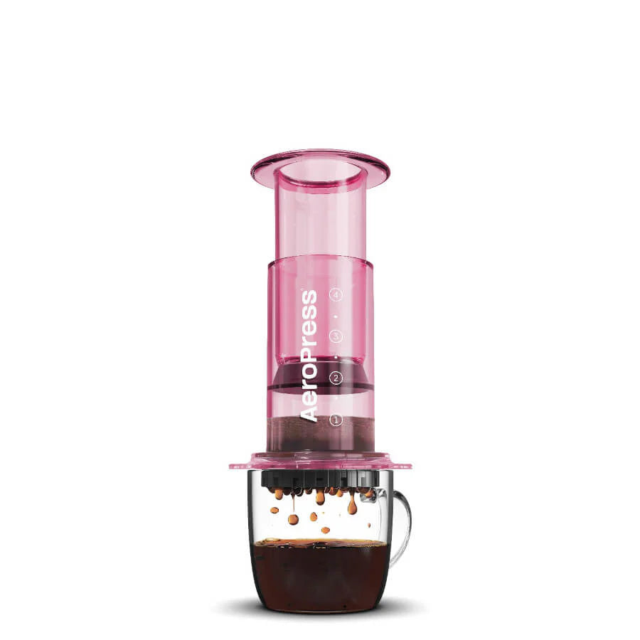 En Pink-limited AeroPress, Clear fra Aeropress brygger kaffe i et halvt gennemsigtigt krus på en hvid baggrund, hvilket fremhæver dens innovative bryggeteknologi.