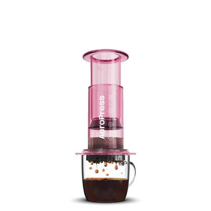 En Pink-limited AeroPress, Clear fra Aeropress brygger kaffe i et halvt gennemsigtigt krus på en hvid baggrund, hvilket fremhæver dens innovative bryggeteknologi.