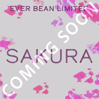 Lysegrå baggrund med pink blomsterstænk, lilla "EverBean Limited Sakura"-tekst og et hvidt diagonalt "COMING SOON"-overlay. Indeholder Sakura-kaffe fremstillet af 100 % Arabica-bønner.