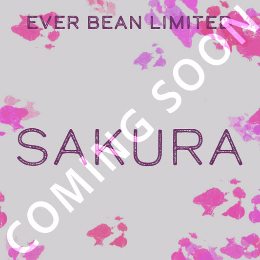 Lysegrå baggrund med pink blomsterstænk, lilla "EverBean Limited Sakura"-tekst og et hvidt diagonalt "COMING SOON"-overlay. Indeholder Sakura-kaffe fremstillet af 100 % Arabica-bønner.