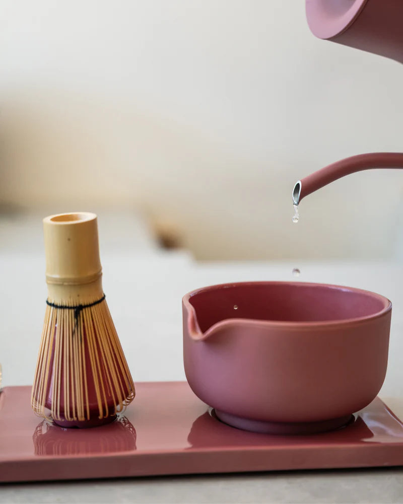 Fellow Matcha-sættet – »Komplet Matcha Sæt« fra Fellow består af en bambuspisk og en lyserød røreskål på et matchende bakke, mens vandet løber fra tekanden og fremhæver mærkets elegante te-ritual.